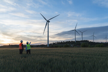 Unrecognized engineers wearing safety helmets working in wind turbine farm during the evening.