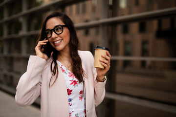 Young businesswoman talking to the phone. Female manager drinking coffee while walking through the city