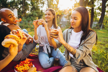 Friends enjoying barbecue time, eating burgers in nature on warm summer day