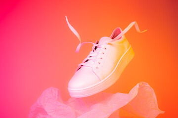 Fashion - white leather sneakers shoe levitating on the pink and orange background