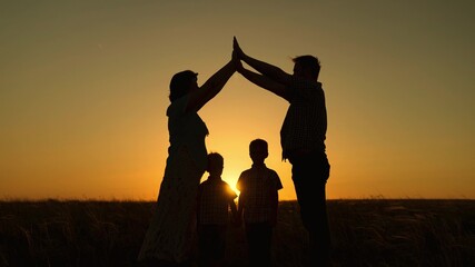 Fototapeta na wymiar Happy family dreams of their own home in park in summer in sunshine. Children mom and dad are playing together building house with their hands, silhouette at sunset. Taking care of children by parents