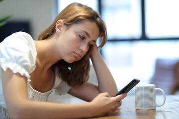 Frustrated and bored woman using smart phone at home