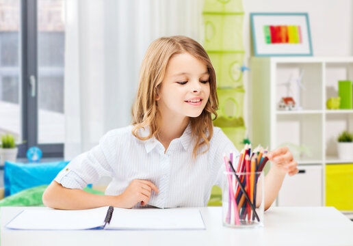 education and school concept - happy smiling student girl drawing with pencils over home room background
