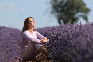 Woman breathing fresh air sitting in a lavender field - obrazy, fototapety, plakaty