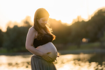 Sunset light illuminating a pregnant woman while looking and touching her belly