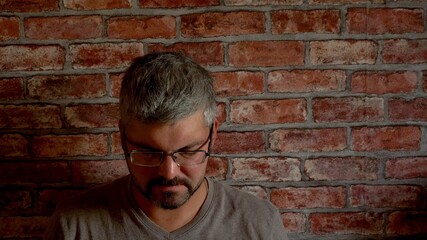 Obraz premium A man with a beard sits against a brick wall. Sad face. Business problems. Loss of a loved one. He dropped his head. Grey hair. Adult. Close-up.