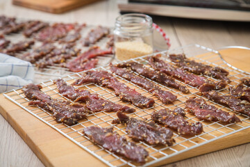 Asia Marinierte Rindfleisch Streifen roh für hausgemachtes Beef Jerky Trockenfleisch mit Sesam und Chili auf Edelstahl Trockengitter für Dörrautomat in Küche mit Holz Brett Hintergrund hell