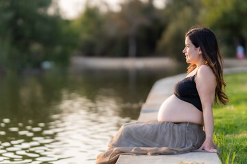 Fototapeta na wymiar Pregnant woman contemplating the river of a park while sitting during sunset