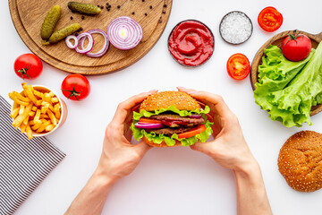 Female hands holding sandwich burger with ingredients. Fastfood meal background