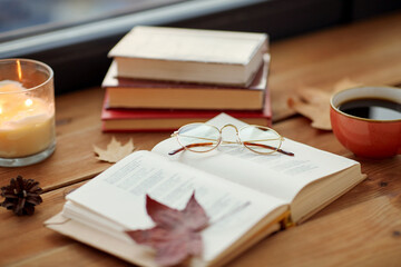 season, leisure and objects concept - open book, cup of coffee, autumn leaves and candle on window...