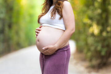 Close-up view of the hands of a adult pregnant woman in her belly outdoors