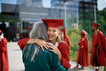 Portrait of cheerful university student hugging mother outdoors, graduation concept.