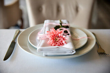 Cloth napkin with pink chrysanthemum lie on a plate in a restaurant. Close-up, selective focus