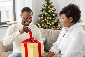 holidays, celebration and people concept - happy african american couple with christmas gift at home