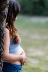 Fototapeta premium Vertical photo of the profile of a pregnant woman leaning on a tree in a park