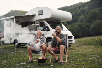 Mature man with senior father talking at campsite outdoors, barbecue on caravan holiday trip. - obrazy, fototapety, plakaty