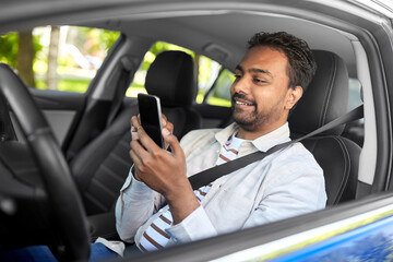 transport, people and technology concept - smiling indian man or driver using smartphone in car
