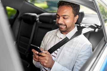 transportation, technology and people concept - smiling indian male passenger with smartphone in taxi car
