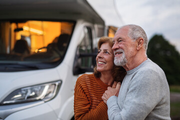 Senior couple standing and hugging outdoors at dusk, caravan holiday trip.