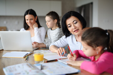 Happy small girls with mother and grandmother using laptop indoors at home, home office and homework concept.