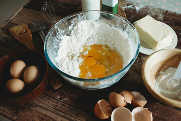 Baking ingredients on wooden table.Healthy homemade recipe for breakfast.Pastry and culinary.Flour and egg yolks in glass bowl.Milk bottle, whisker and butter.Home bake space.Pizza dough.