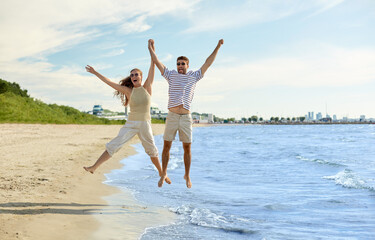leisure, relationships and people concept - happy couple jumping on summer beach