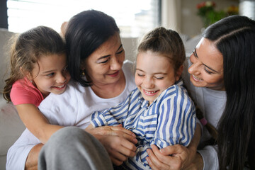 Happy small girls with mother and grandmother indoors at home, hugging.