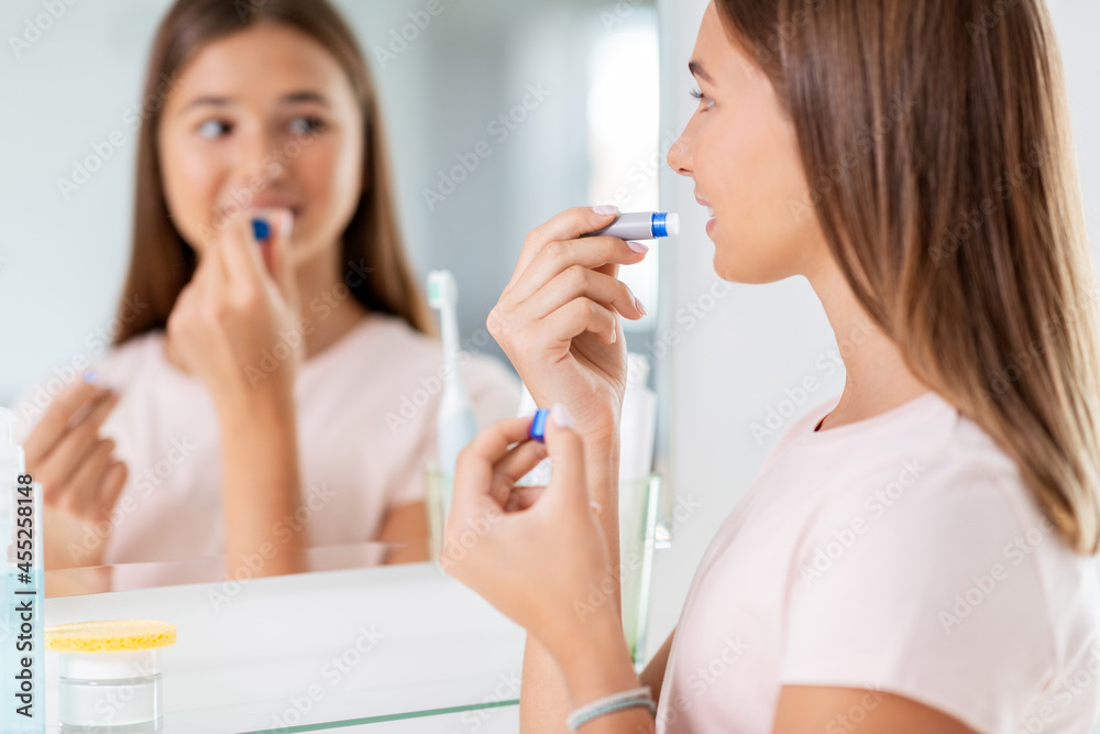 Canvas Prints beauty and cosmetics concept - teenage girl applying lip balm and looking to mirror at home bathroom