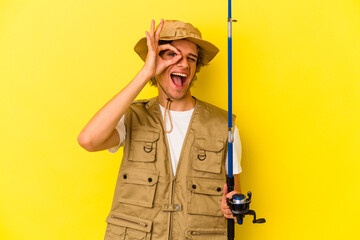 Young fisherman with makeup holding rod isolated on yellow background  excited keeping ok gesture on eye.