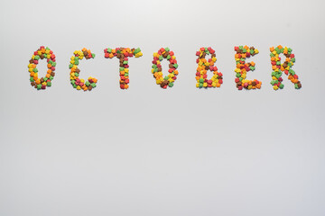October inscription on a white background. Confectionery sprinkles in the form of multi-colored maple leaves
