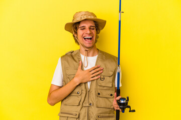 Young fisherman with makeup holding rod isolated on yellow background  laughs out loudly keeping hand on chest.