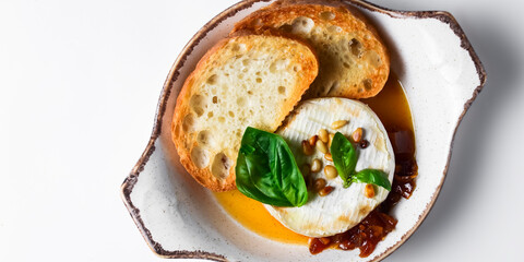 Baked camembert with sauce and toast served in a white bowl over white background. Delicious dinner idea