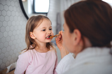 Mother with small daughter brushing teeth indoors in bathroom in the evening or morning.