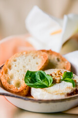 Baked camembert with sauce and toast served in a white bowl over beige cloth background. Delicious dinner idea