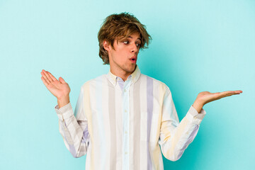 Young caucasian man with make up isolated on blue background  confused and doubtful shrugging...