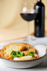 Baked camembert with sauce and toast served in a white bowl over beige cloth background. Delicious dinner idea