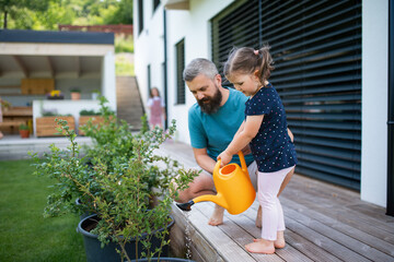 Father and small daughter outdoors in tha backyard, watering plants.