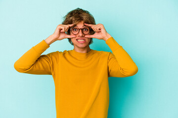 Young caucasian man with make up isolated on blue background  keeping eyes opened to find a success opportunity.