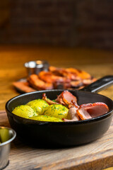 Fried rustic potatoes with bacon and sausages in a pan close-up. Over wooden background.