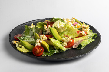 Plate of fresh and healthy summer avocado and tomatoes salad with fresh greenery and popcorn.