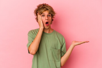 Young caucasian man with make up isolated on pink background impressed holding copy space on palm.