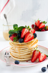 Breakfast pancakes. Stack of pancakes with fresh blueberries and strawberries on plate with bowls of strawberries and blueberries on light slate, stone or concrete background. Top view. copy space