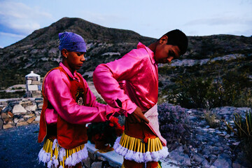 Two male traditional mexican dancers getting ready. One helping the other