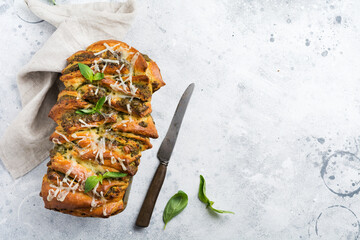 Homemade braided pesto bread garnished with basil leaves on a simple light grey concrete table....