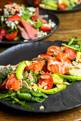 Salad with salmon, avocado and tomatoes served on a black plate. Italian cuisine concept