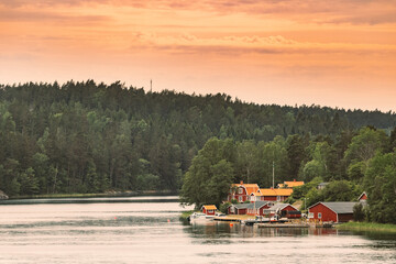 Sweden. Many Beautiful Red Swedish Wooden Log Cabins Houses On Rocky Island Coast. Lake Or River Landscape