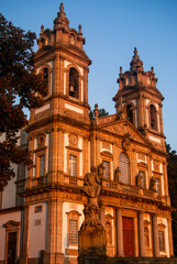 Fototapeta na wymiar Beautiful church and a statue turn orange at sunset with beautiful clear sky - Vertcal, Bom Jesus, Braga, Portugal