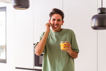 Young mixed race man drinking orange juice in his kitchen covering ears with hands.