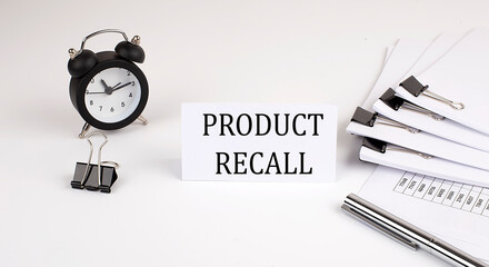Card with text PRODUCT RECALL on a white background, near office supplies and alarm clock. Business...