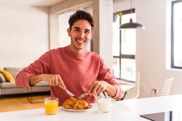 Obraz na płótnie Canvas Young mixed race man eating croissant in a kitchen on the morning